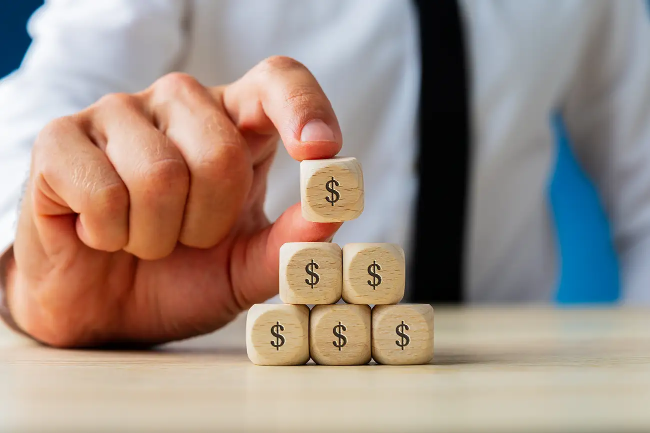 An AdvantEdge Local team member placing a wooden block with a dollar sign on top of other wooden blocks with dollar signs as a metaphor for PPC campaigns being optimized and making money